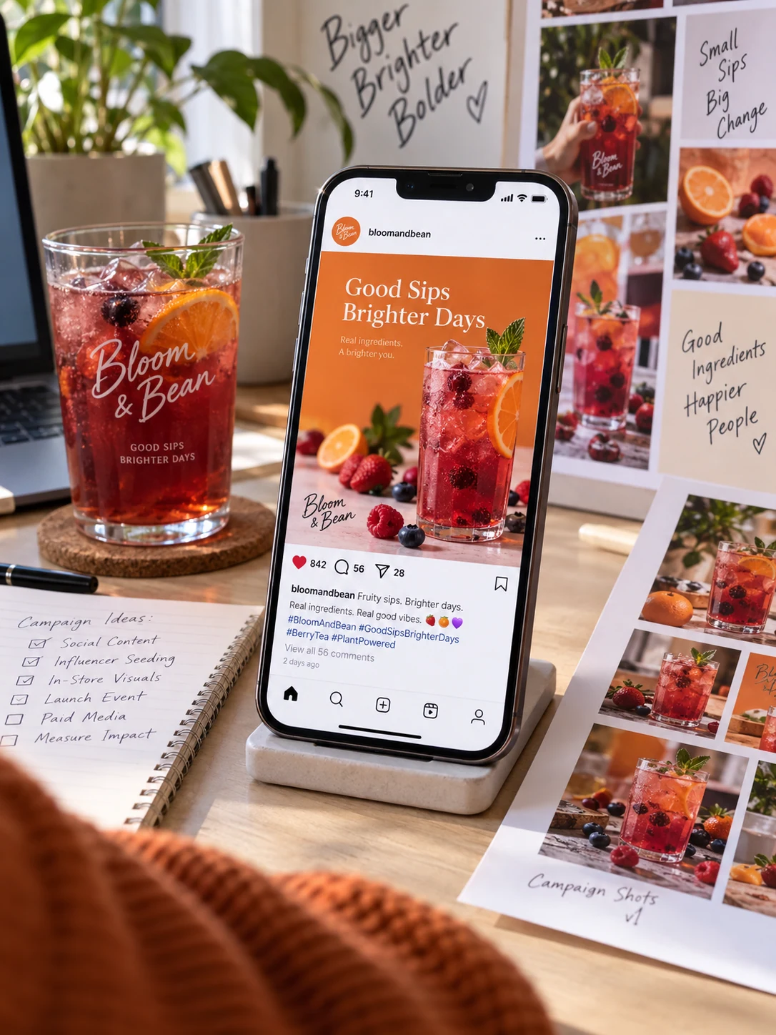 Close diagonal view of a smartphone standing upright on a small desk stand showing a vivid fictional 'Bloom & Bean' social media beverage campaign