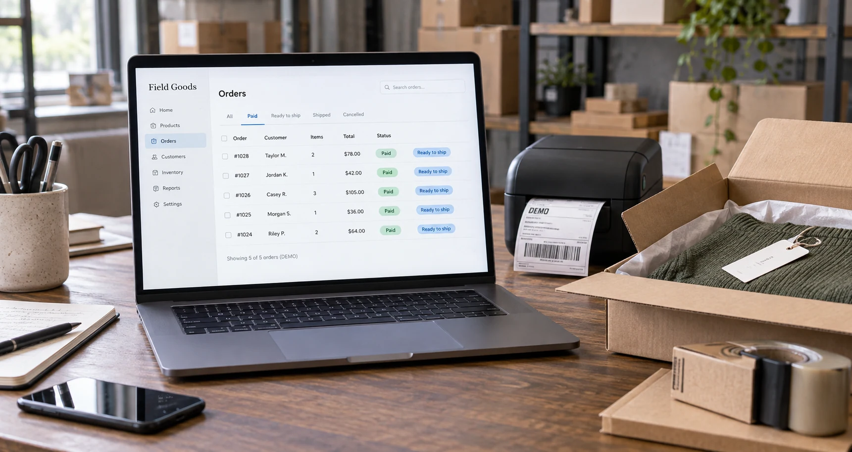 Wide merchant workbench: laptop showing 'Field Goods / Orders / Paid / Ready to ship / DEMO', an open product package and label printer